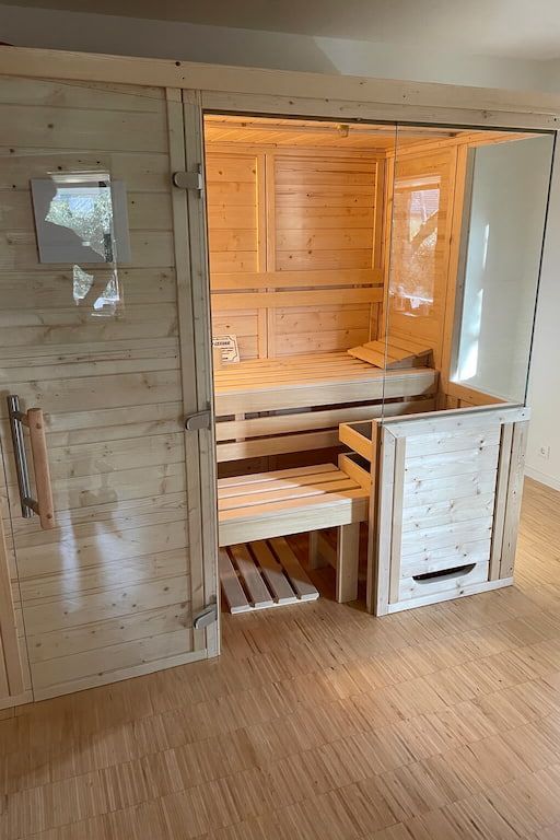 Moderne Bormio Massivholzsauna aus hellem Fichtenholz mit großer Glasfront, massiven Saunabänken und klassischer Wellness-Atmosphäre im Innenbereich