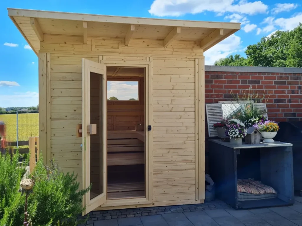 Klassische Gartensauna aus hellem Massivholz mit überdachtem Dach und gemütlicher Wellness-Atmosphäre im Garten
